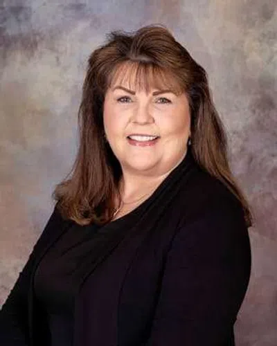 Smiling woman with shoulder-length brown hair wearing black clothing against a neutral background.