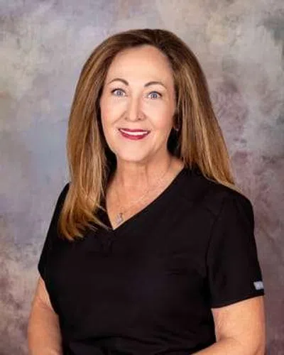 Smiling woman with long brown hair wearing a black shirt against a soft gray background