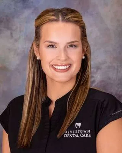 Smiling dental professional in Rivertown Dental Care uniform against a blurred gray background