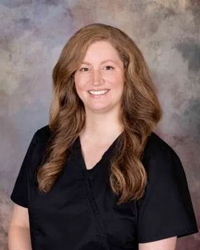 Smiling woman with long wavy hair wearing black medical scrubs against a neutral backdrop