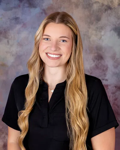 Smiling young woman with long blonde wavy hair wearing a black shirt against a mottled background