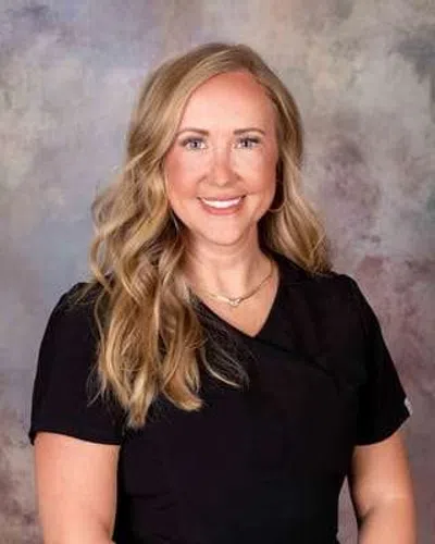 Smiling woman with long blonde hair wearing a black top against a neutral textured background
