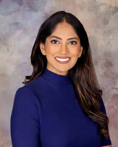 Smiling woman with long dark hair wearing a blue turtleneck against gray patterned background.
