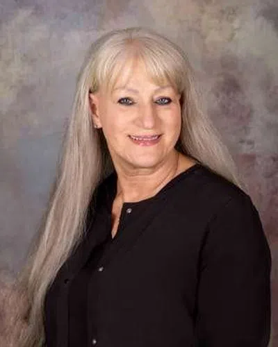 Smiling older woman with long blonde hair wearing a black blouse against a mottled gray background