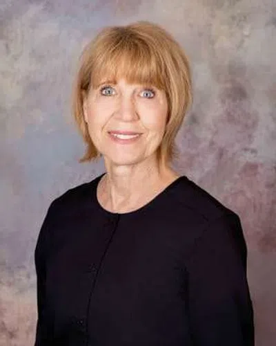 Smiling middle-aged woman with short blonde hair wearing a black top against a muted textured background.