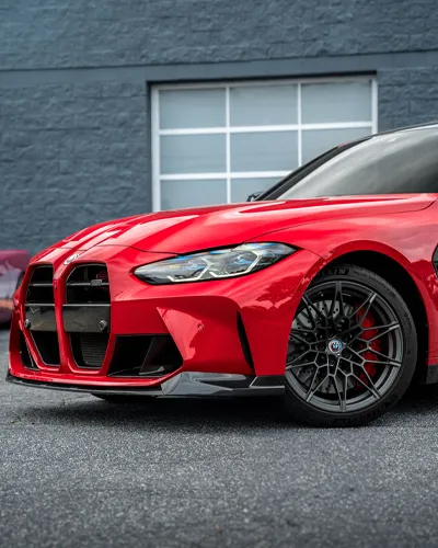 Close-up of a red sports car front with aggressive grille and black alloy wheels parked on asphalt.