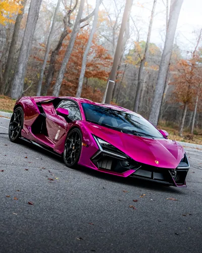 Vibrant magenta luxury sports car parked on road with autumn trees in the background.