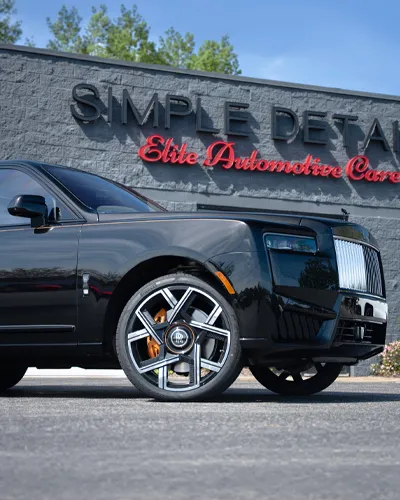Black luxury Rolls-Royce parked in front of Simple Detail Elite Automotive Care building on a sunny day.
