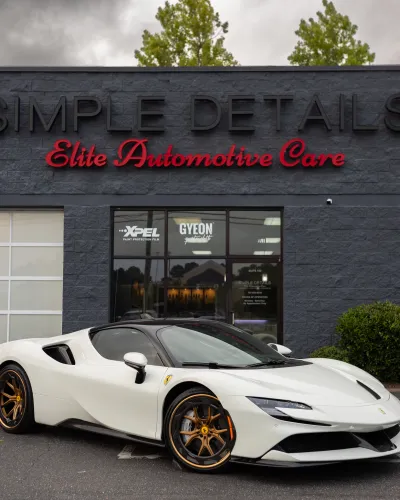 White Ferrari sports car with bronze wheels parked in front of Simple Details Elite Automotive Care building.