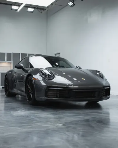 Sleek dark gray Porsche sports car parked in a clean, modern garage with polished concrete floor and cabinetry.