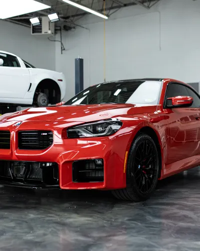 Sleek red sports car parked in a modern garage with a white car raised on a lift in the background.