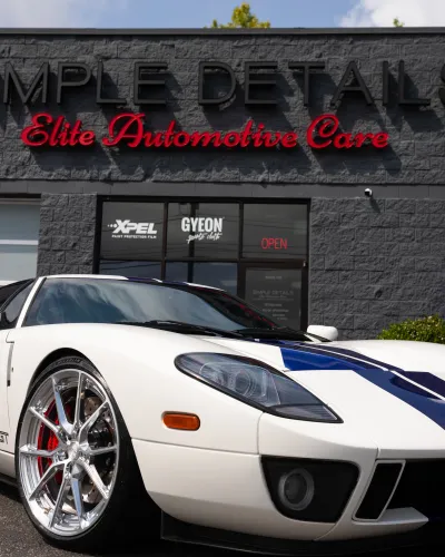 White Ford GT with blue racing stripes parked in front of Simple Details Elite Automotive Care shop.