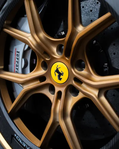Close-up of a gold Ferrari alloy wheel with carbon fiber rim and branded brake caliper on a sports car.