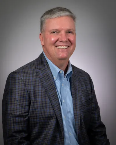 Smiling middle-aged man in a blue checkered blazer and light blue shirt against a gray background