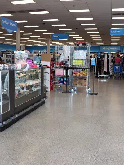 Inside a spacious thrift store with sections for juniors, dresses, and fitting rooms, and a staff member at a glass counter.