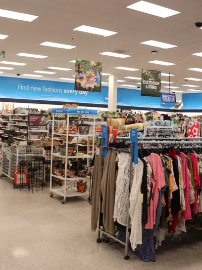 Interior of a brightly lit store with clothing racks and signage for fashion and outdoor living sections.
