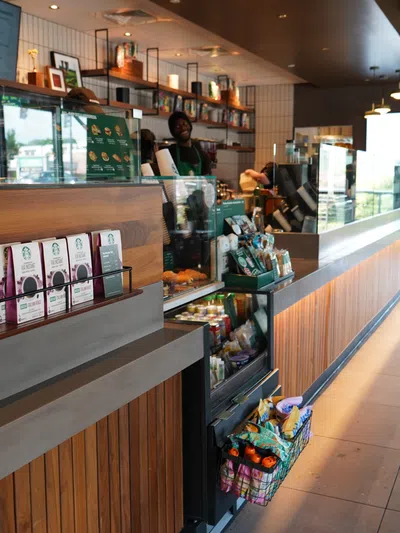 Modern Starbucks café interior with wooden counter, packaged coffee products, and baristas serving customers.