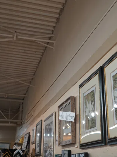 Gallery wall with framed artwork and photos illuminated by ceiling track lighting in an art sale exhibition space.