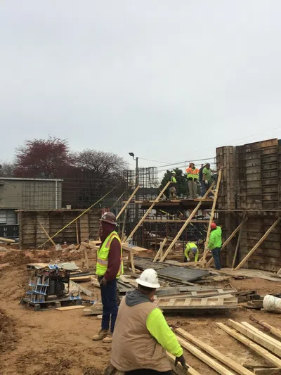 Construction workers in high-visibility clothing building wooden framework on a cloudy day at a construction site.