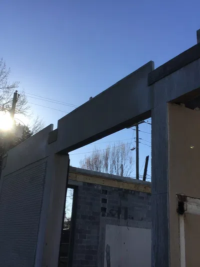 Partially constructed concrete building with clear blue sky and sun shining through trees in the background