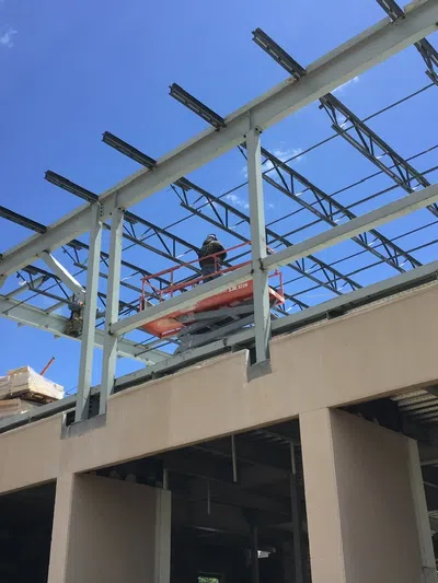 Construction worker on lift working on steel frame of building under clear blue sky.
