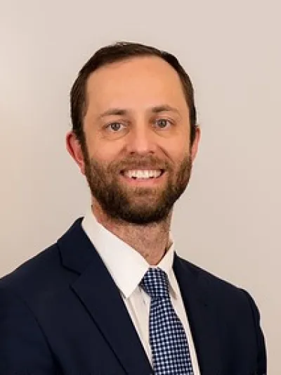 Smiling man in navy suit and checkered tie against a plain light background professional headshot