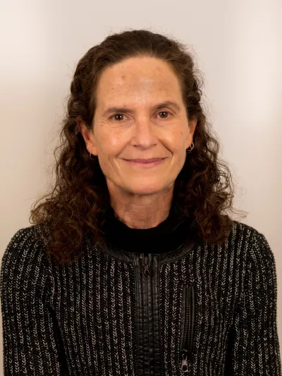 Middle-aged woman with curly brown hair wearing a black and gray textured sweater against a plain backdrop.
