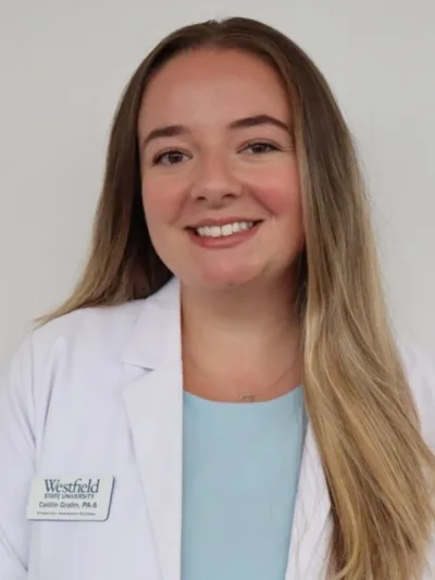 Smiling healthcare professional in a white coat with a Westfield State University name badge against a plain background