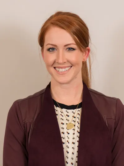 Smiling woman with red hair wearing a maroon jacket and polka dot blouse