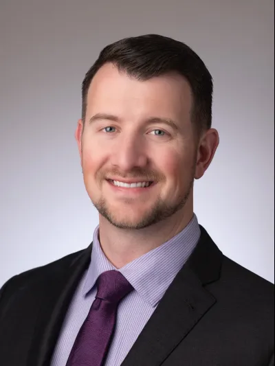 Professional man in suit with purple tie smiling against a neutral background, business portrait