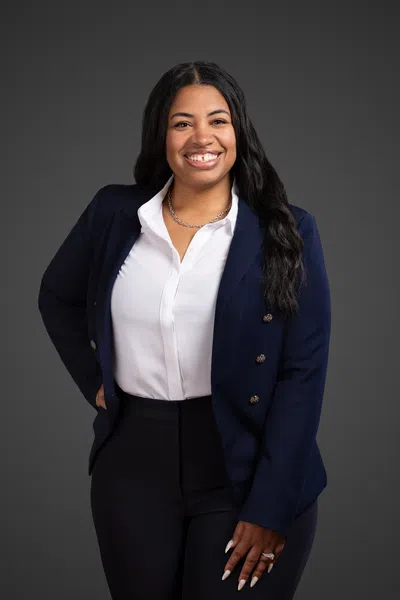 Confident woman wearing a navy blazer and white blouse smiling against a dark gray background.