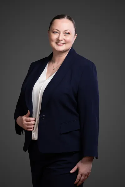 Smiling woman in navy blazer and white blouse posing confidently against a dark gray background.