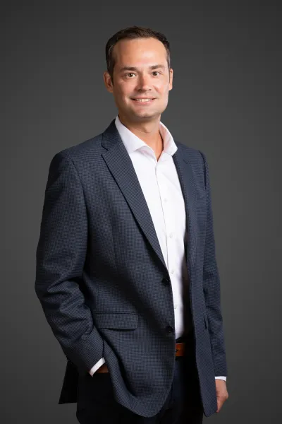 Professional man in a navy checkered blazer and white shirt smiling against a dark gray background.