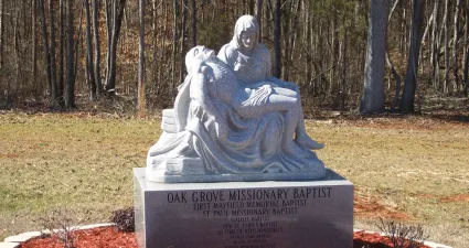 a statue of a person sitting on a rock in a park