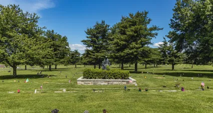 a grassy area with trees and a statue in the middle