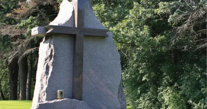 a statue of a person with a cross on a stone slab in front of trees