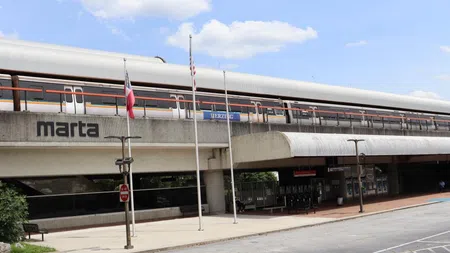 MARTA train traveling above Berzelia station platform with flags and blue sky in Atlanta