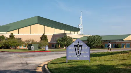 Christian Academy campus with green-roofed buildings, directional sign, trees, and a person walking on a sunny day.