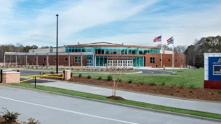Modern Legacy Arena building with flags, green lawn, and clear blue sky on a sunny day