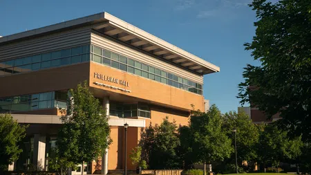 Modern Prillaman Hall with large windows surrounded by green trees under a clear blue sky.