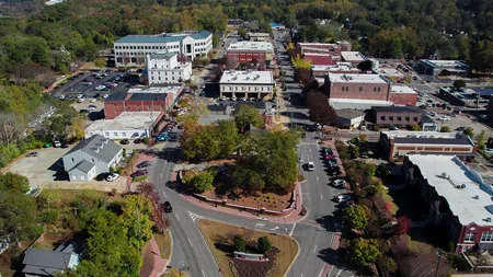 Aerial view of a small town center with classic buildings, tree-lined streets, and a central roundabout park.