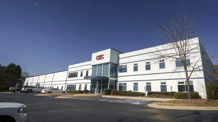 Modern white two-story commercial building with GEC logo under clear blue sky and empty parking lot.