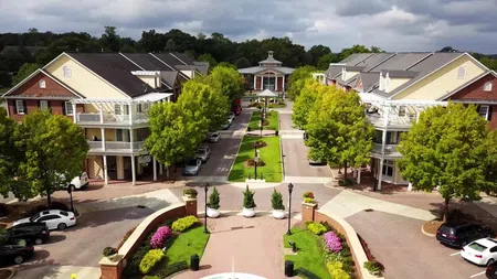 Aerial view of a residential area with townhouses, greenery, parked cars, and a central walkway under a cloudy sky