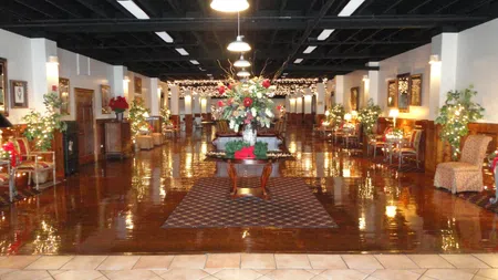 Spacious elegant lobby with polished wooden floors, floral centerpiece, seating, and festive string lights.
