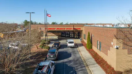 Exterior view of Flowery Branch High School with parked cars and clear blue sky on a sunny day.