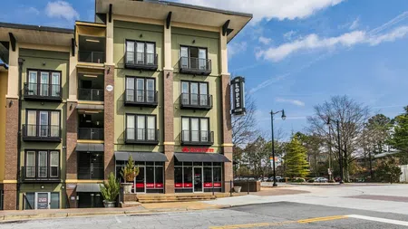 Modern multi-story apartment building with retail space on ground floor under blue sky in urban setting