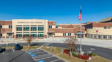 Front view of Gainesville High School with American flag, parking lot, and clear blue sky on a sunny day