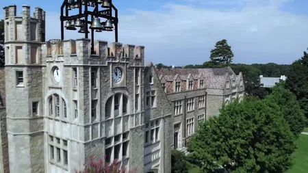 Stone clock tower and historic university building with bell structure surrounded by trees under blue sky