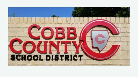 Sign for Cobb County School District on a beige brick wall under a clear blue sky.