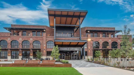 Modern red brick Chamblee City Hall building with large windows, green lawn, and trees under blue sky.